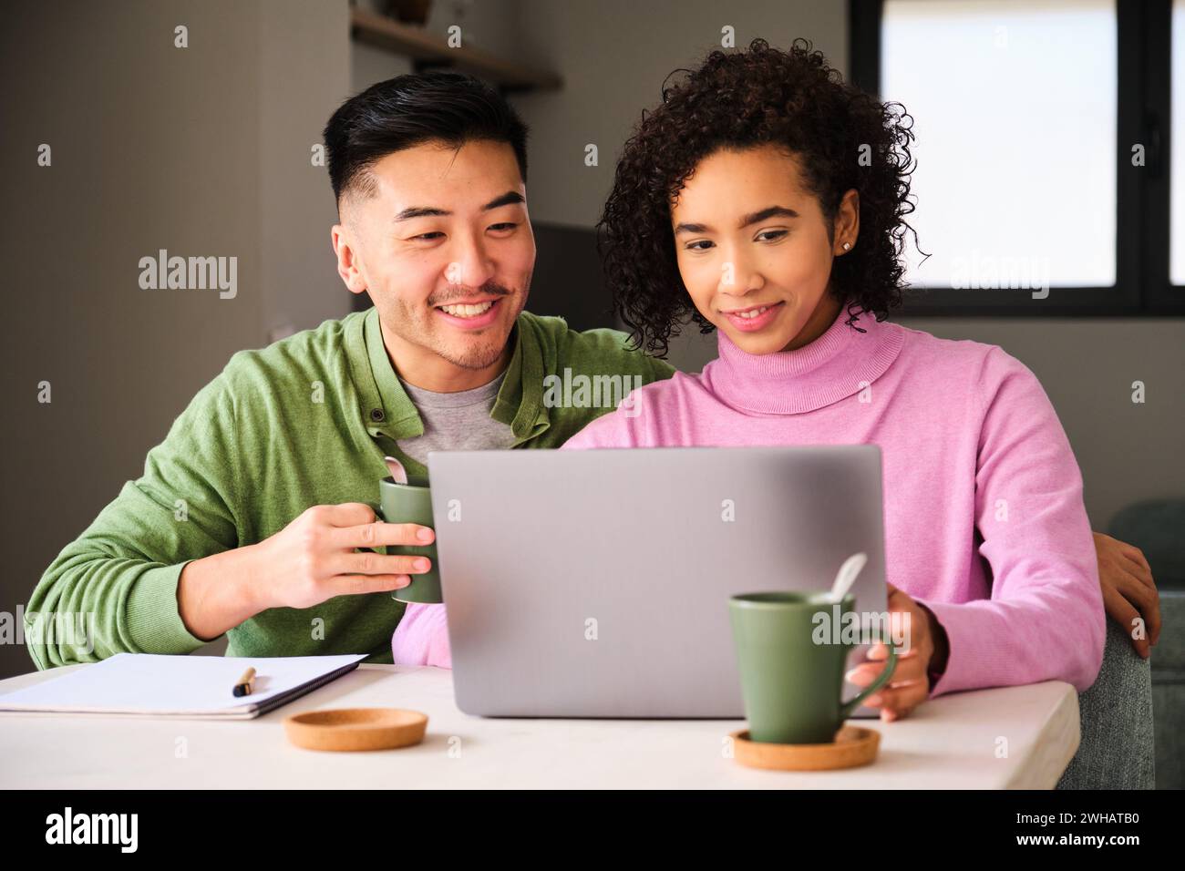 Coppia multietnica sorridente, che usa il portatile e beve caffè. Foto Stock