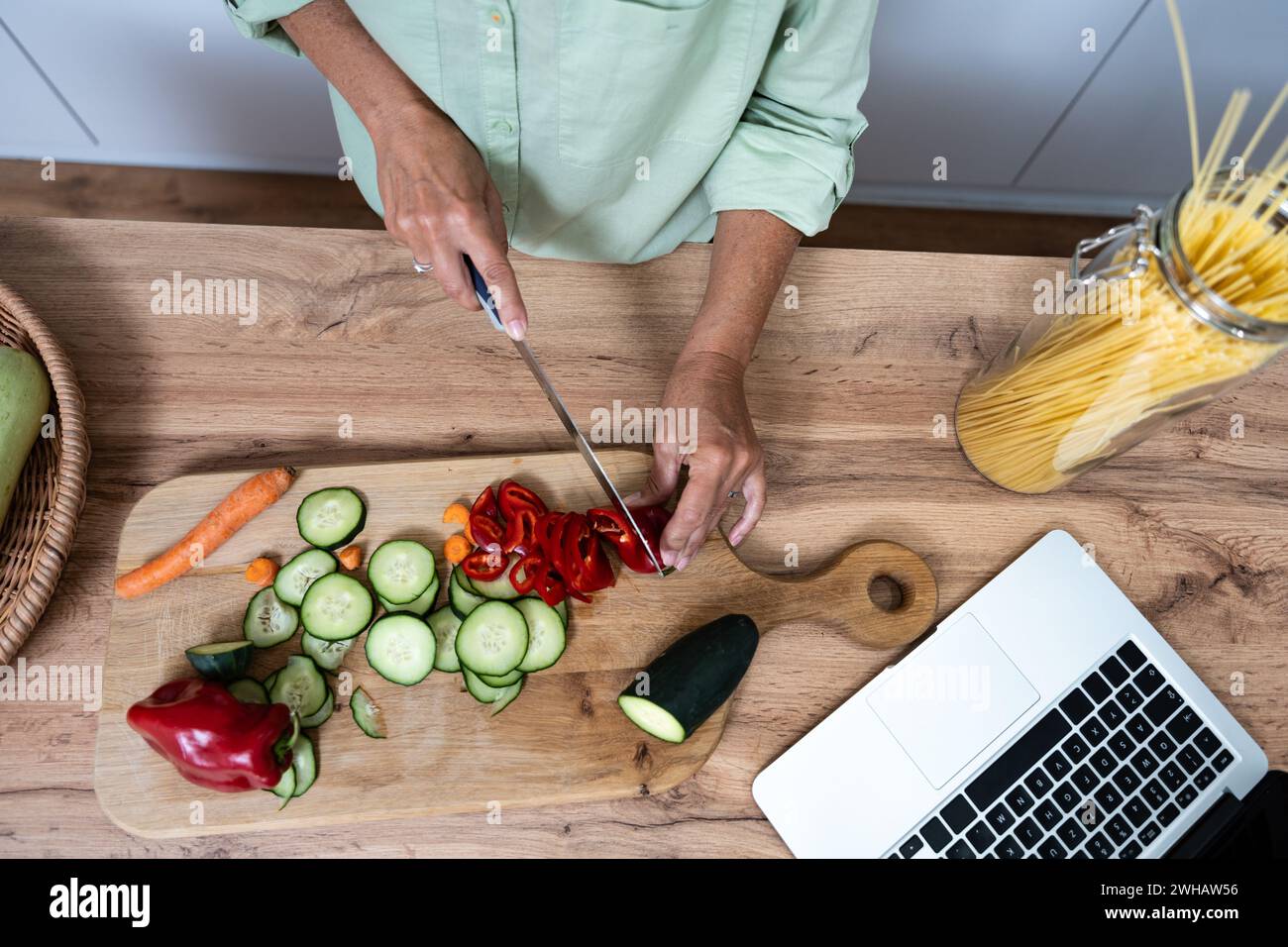 Senior donna sopravvissuto cancro lettura ricette in cucina da computer portatile cucinare sano verdure cibo vegan per una migliore salute e corpo rigenerato Foto Stock