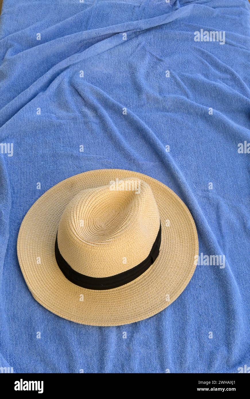 Cappello di paglia appoggiato su un telo da spiaggia blu. Niente persone. Foto Stock