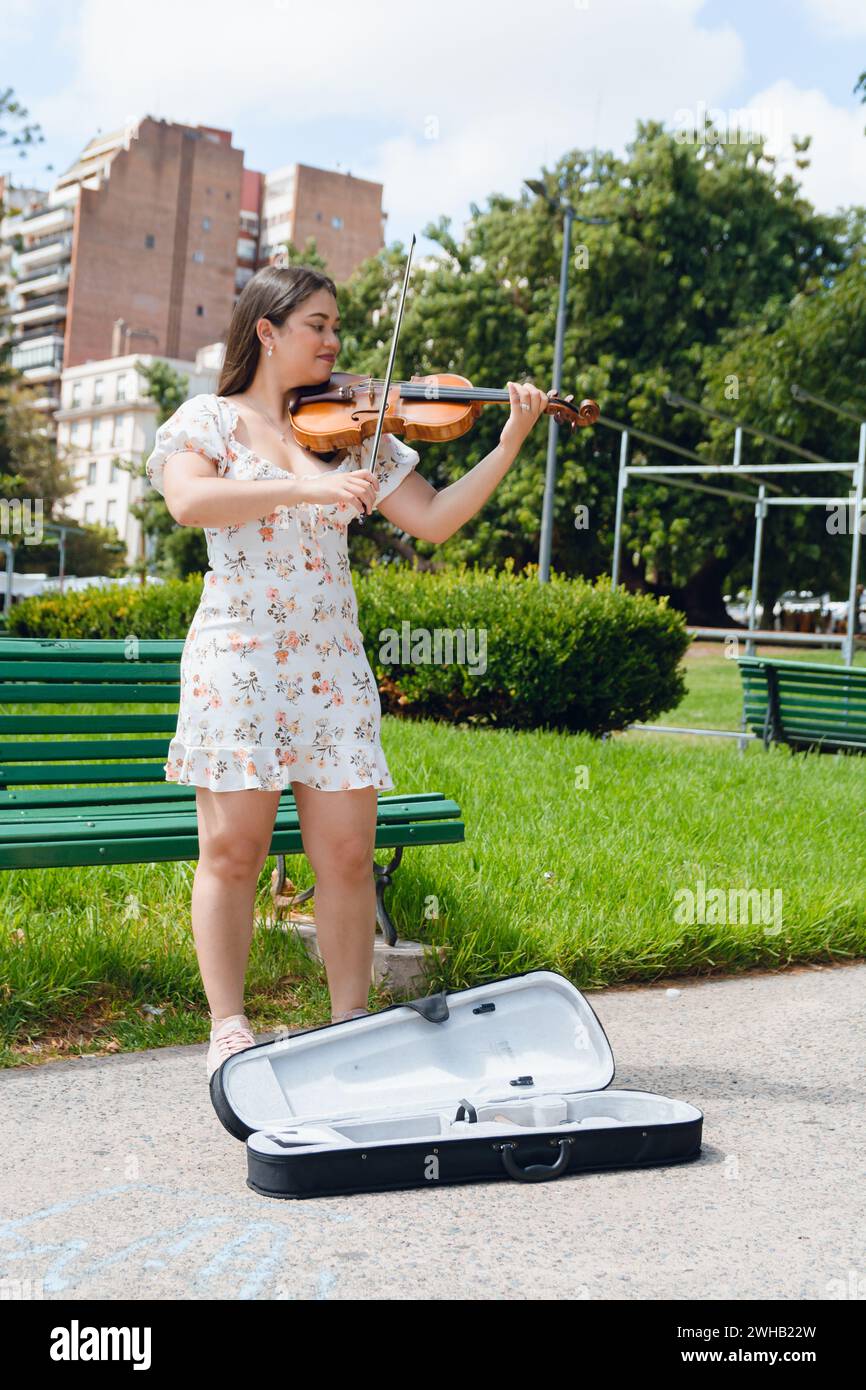 immagine verticale di una giovane donna di busker latina violinista che indossa un abito, capelli lunghi, ha ispirato un felice gioco per strada, facendo musica e lavorando, copiando spazio. Foto Stock