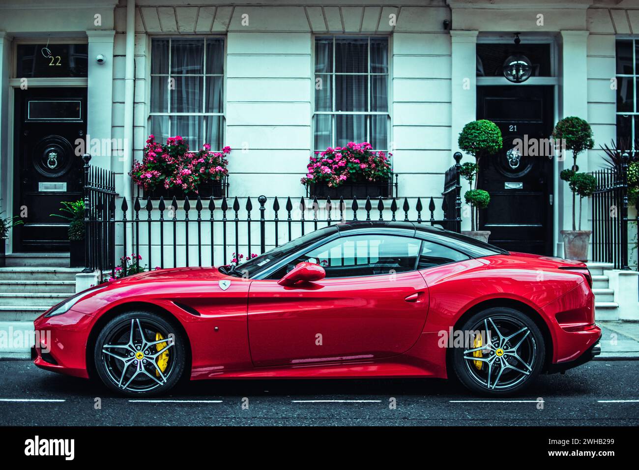 Un'elegante Ferrari rossa parcheggiata in una classica strada londinese, che unisce lusso moderno e fascino urbano storico. Foto Stock