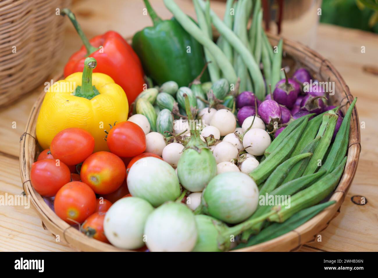 Vivace selezione di verdure fresche, tra cui pomodori, peperoni, melanzane e okra in un cestino rustico di vimini, che mette in mostra prodotti biologici Foto Stock