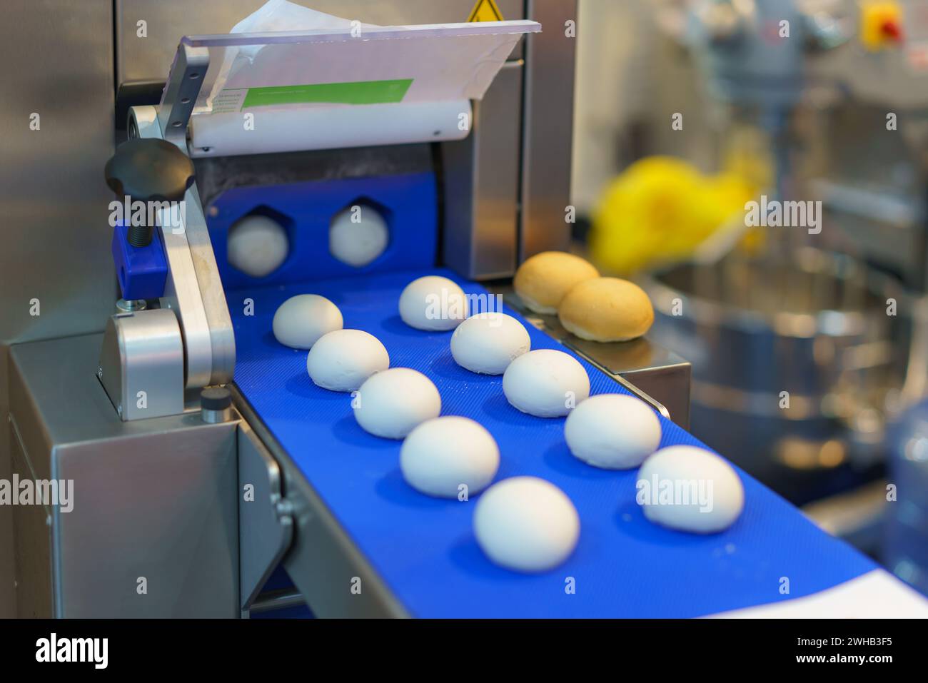 Immagine ravvicinata di un sistema automatizzato di trasformazione alimentare industriale che mostra porzioni di impasto su un nastro trasportatore blu, con elementi di macchinari sul retro Foto Stock