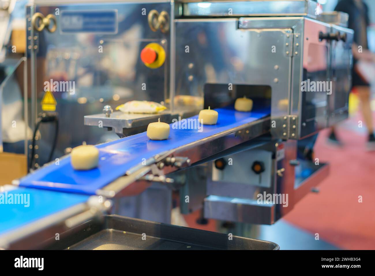 Immagine ravvicinata di un sistema automatizzato di trasformazione alimentare industriale che mostra porzioni di impasto su un nastro trasportatore blu, con elementi di macchinari sul retro Foto Stock