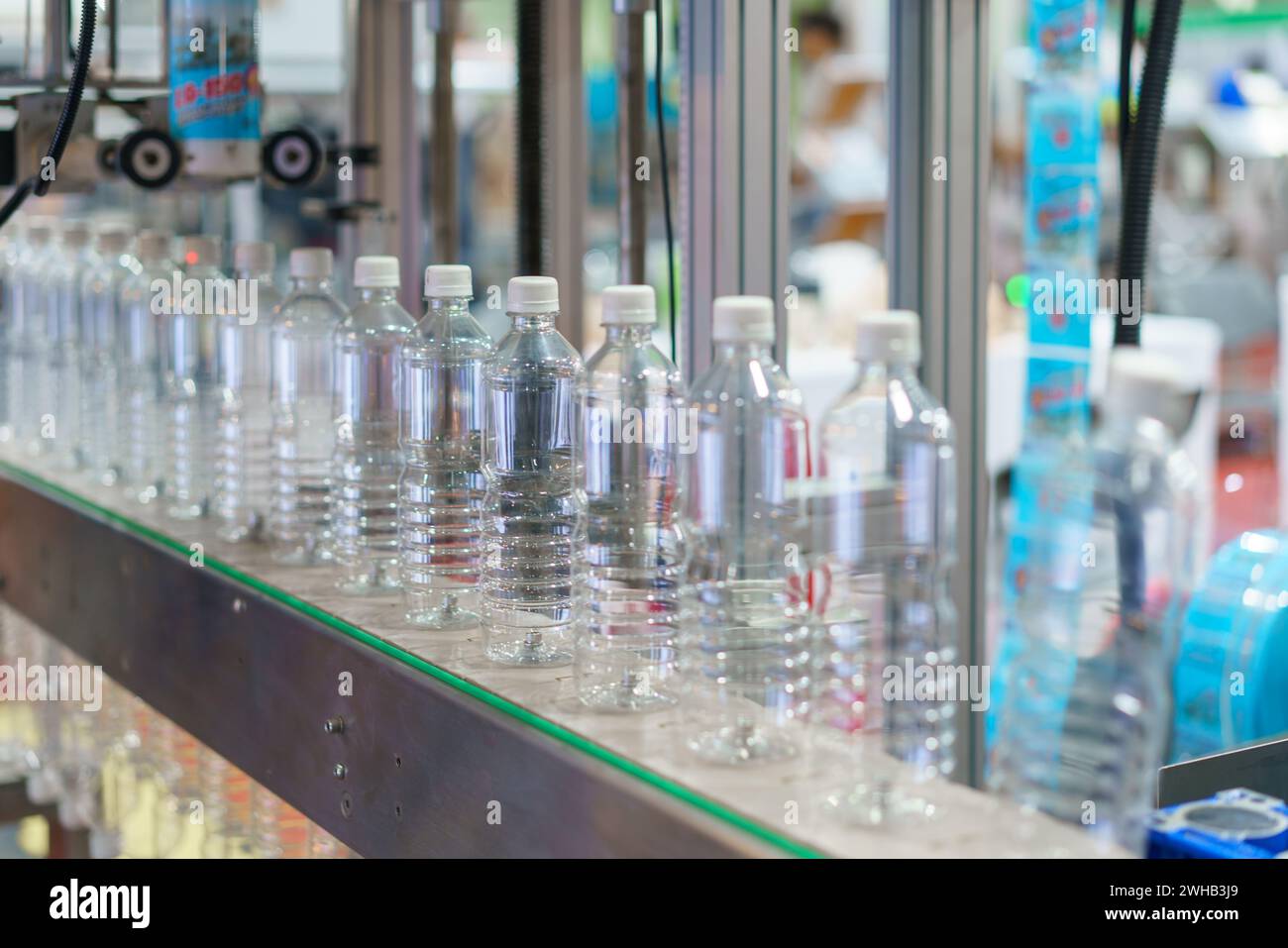 Immagine che mostra una fila di bottiglie d'acqua in plastica trasparente su un nastro trasportatore in un impianto di imbottigliamento, con particolare attenzione alle bottiglie e ai macchinari industriali i. Foto Stock