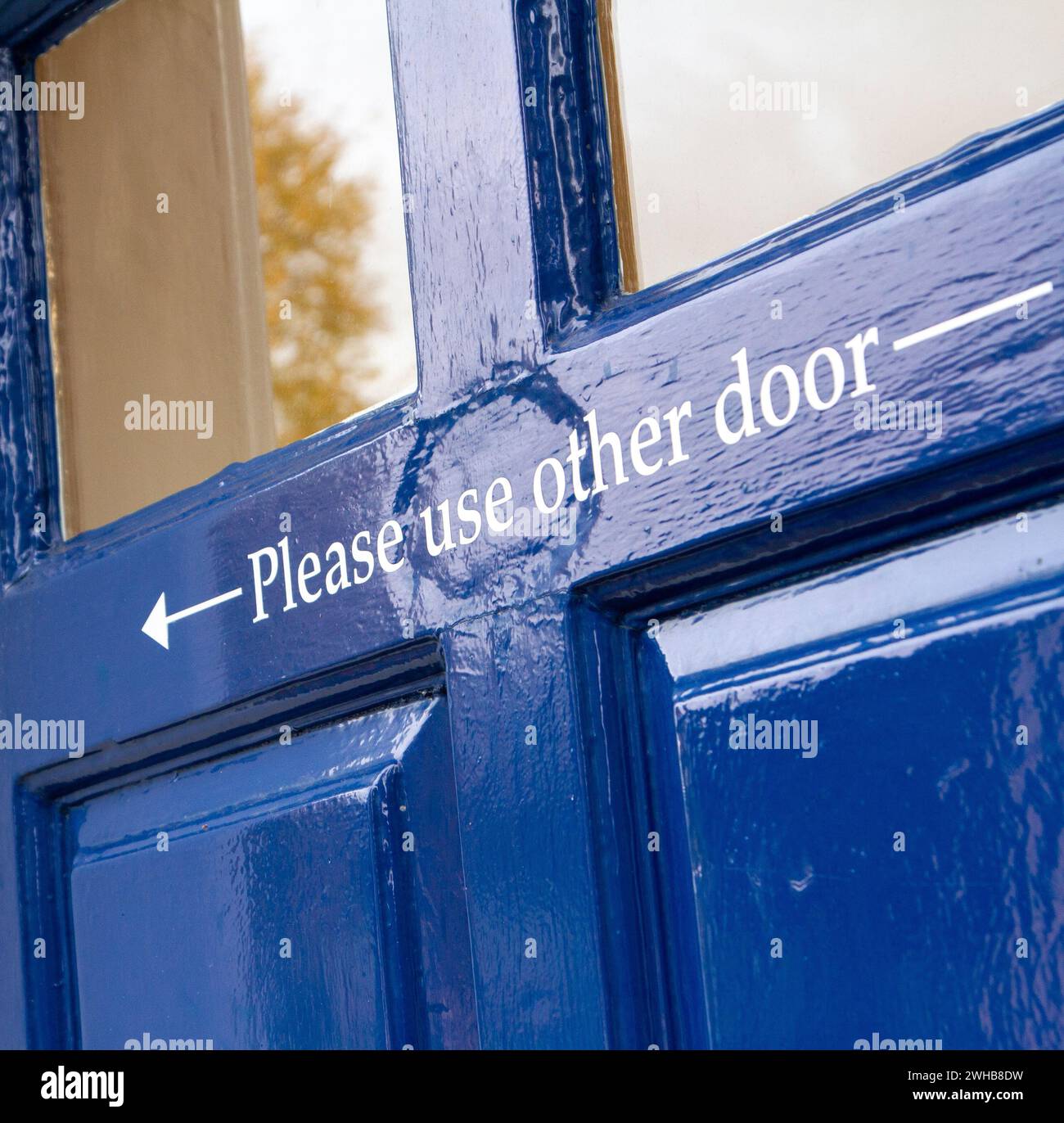 Lo sportello verniciato lucido blu scuro presenta una freccia di direzione e le istruzioni "Please use other door" ... Molto inglese:) Foto Stock