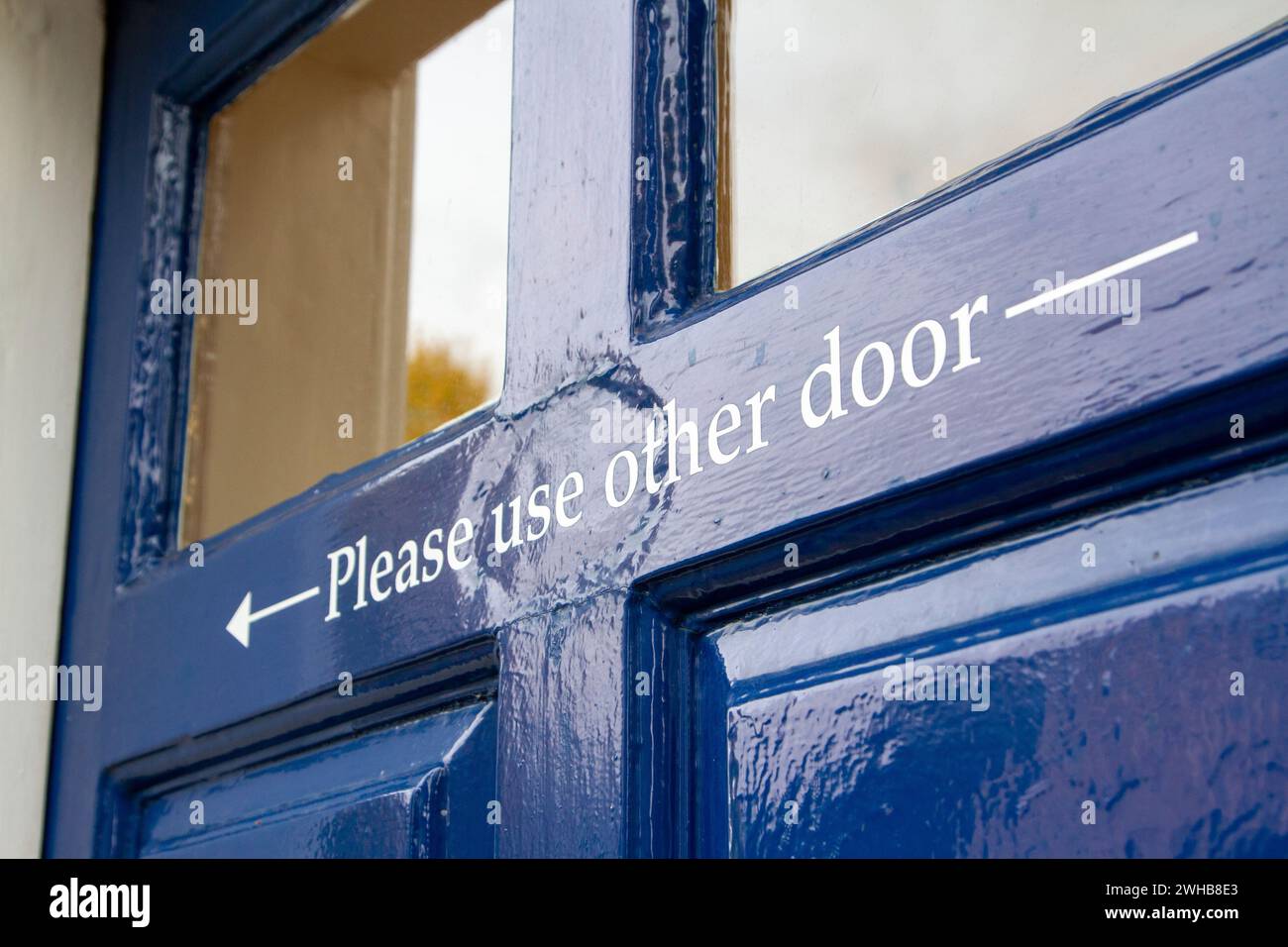 Lo sportello verniciato lucido blu scuro presenta una freccia di direzione e le istruzioni "Please use other door" ... Molto inglese:) Foto Stock