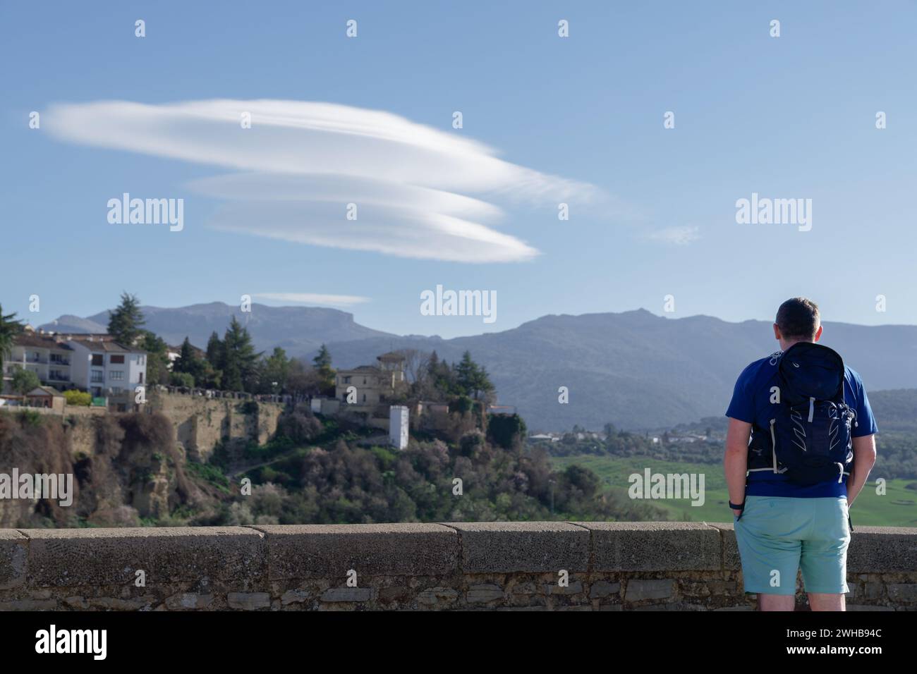 il turista si vede dal retro ammirando un paesaggio idilliaco di un villaggio su una scogliera e un cielo blu con nuvole Foto Stock