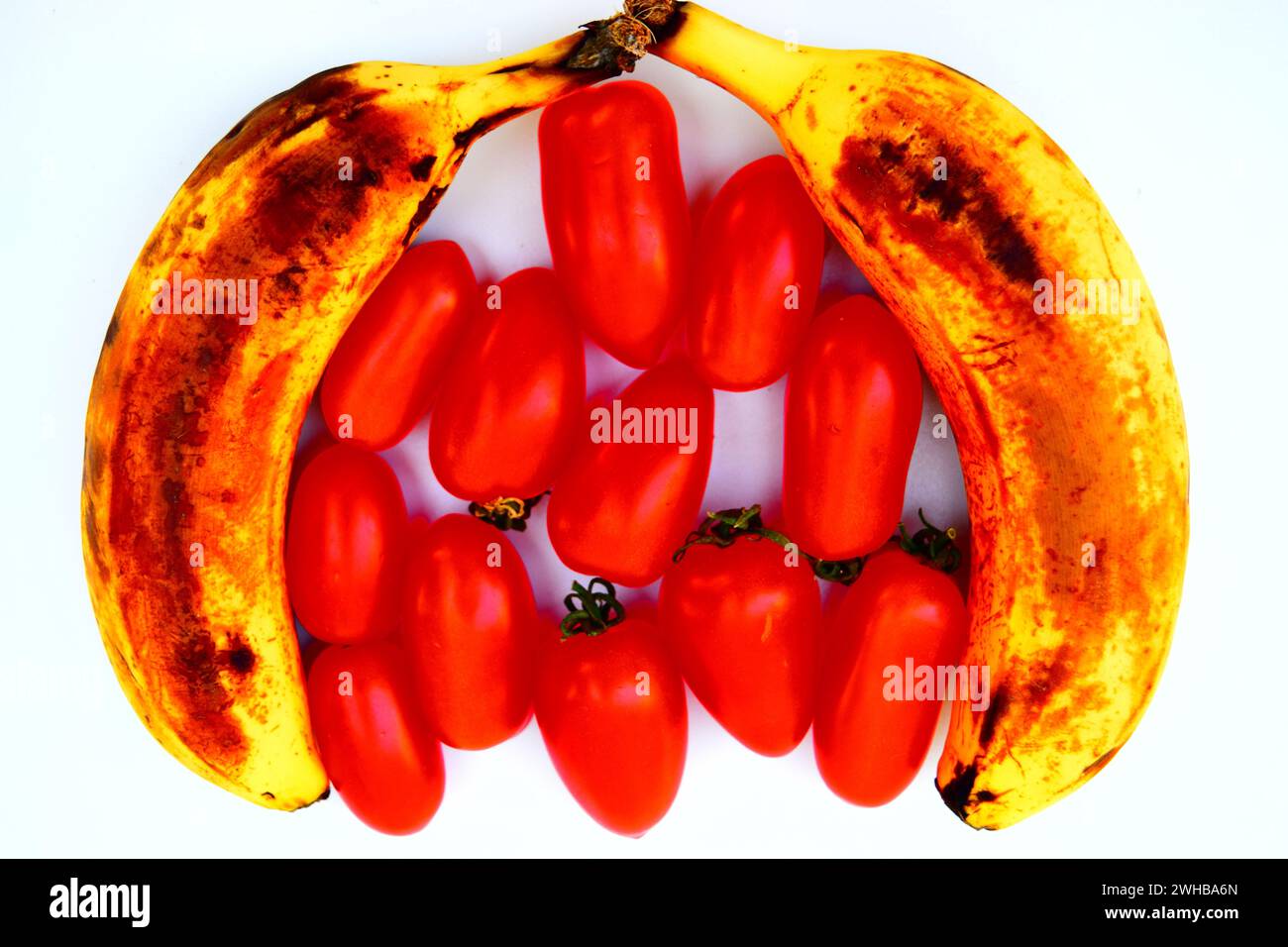 Due banane mature a forma di campana con pomodori rossi al centro. Foto Stock