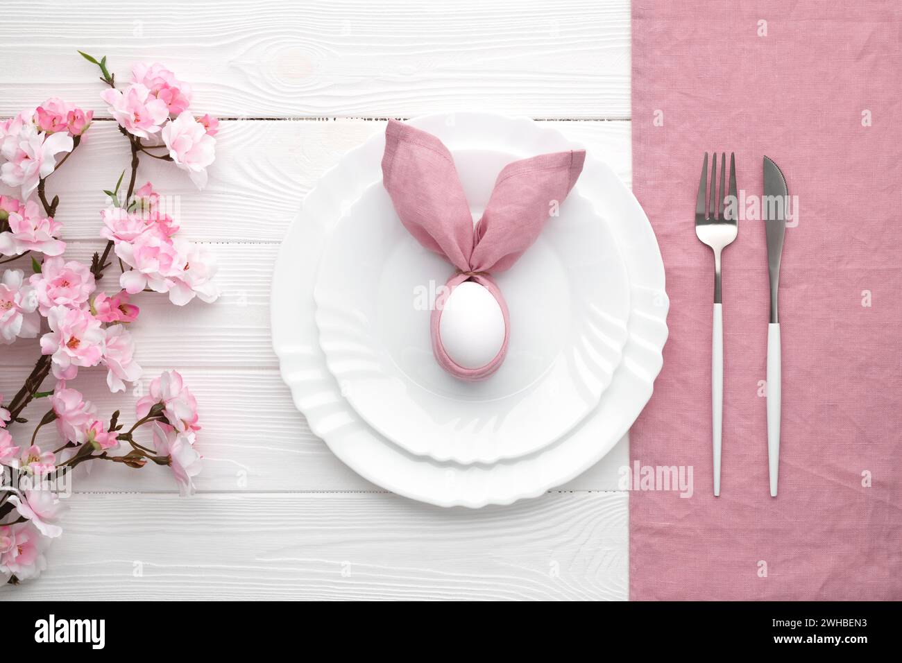Invito al pranzo di Pasqua. Tavolo festivo con fiori primaverili rosa e posate. Coniglietto con tovagliolo di lino e uovo. Buone vacanze di Pasqua, menu co Foto Stock