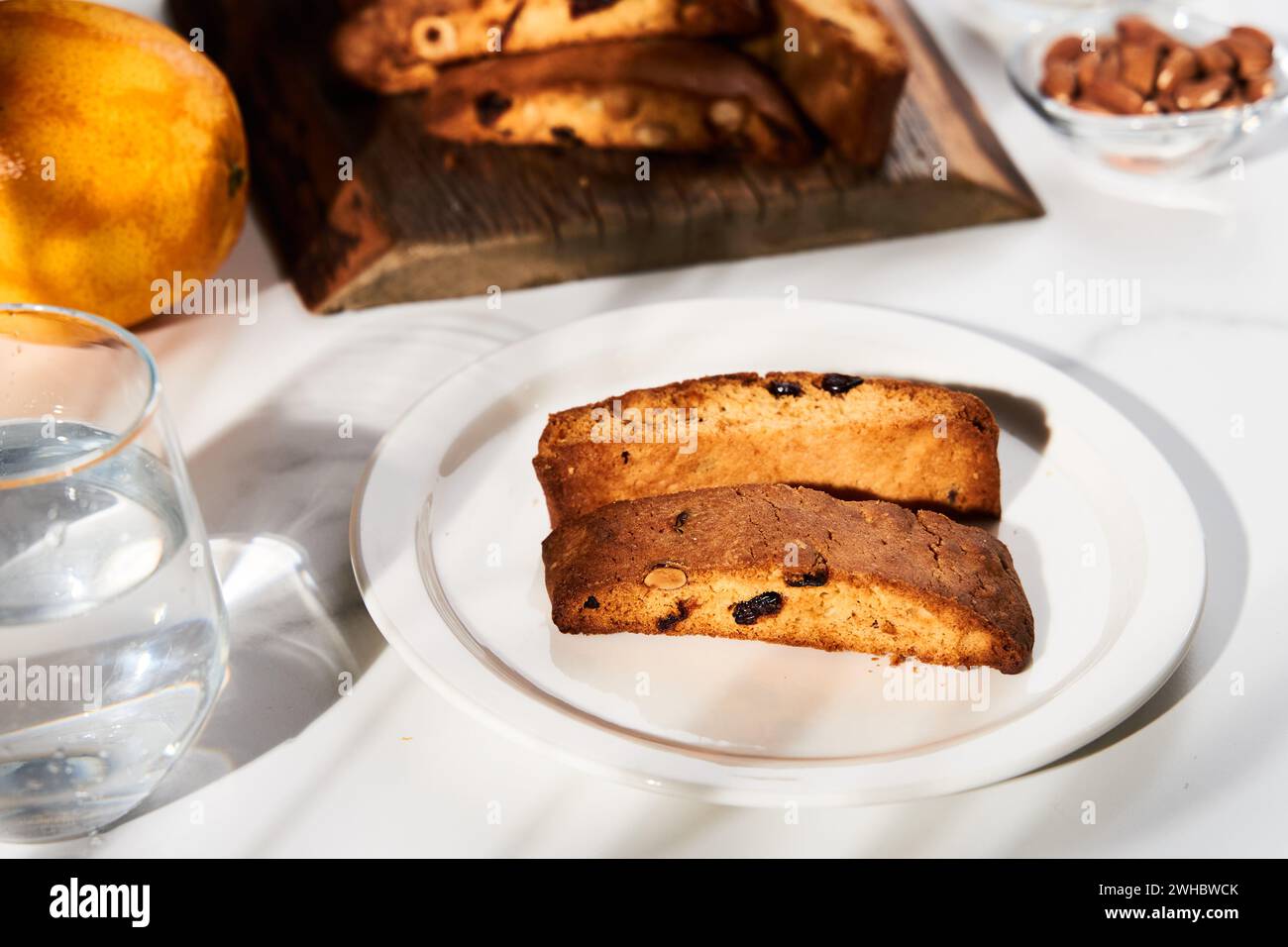 Fette di biscotti di mandorle, nocciole e mirtilli rossi dorati su un elegante piatto bianco, illuminate da luce naturale sulla superficie in marmo Foto Stock