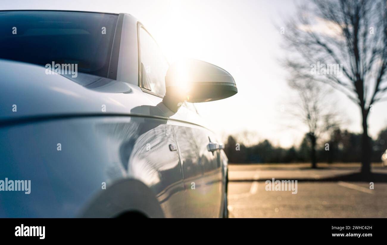 Angolazione ridotta di un'auto bianca con retroilluminazione del sole sullo specchio Foto Stock