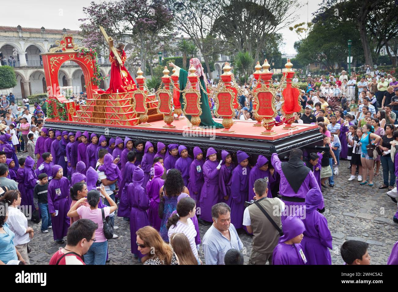 Antigua, Guatemala. Spettatori, famiglia e turisti osservano i ragazzi adolescenti che portano un galleggiante in una processione religiosa durante la settimana Santa, la Semana San Foto Stock