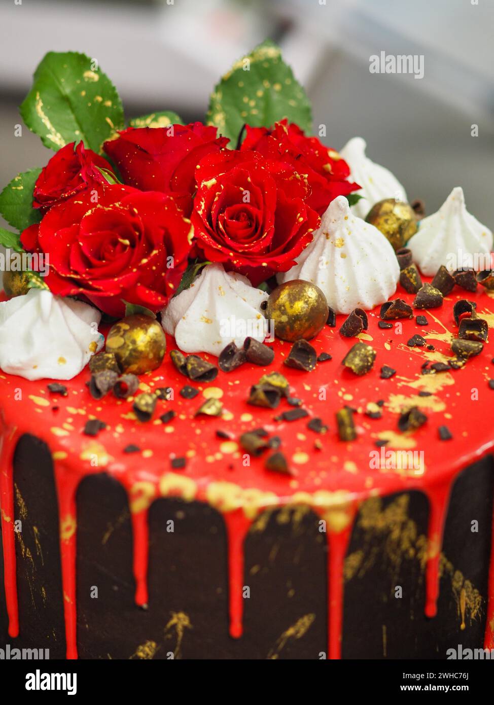 Dettagli laterali di una torta decorata con rose, glassa rossa sgocciolante e dolci al cioccolato Foto Stock