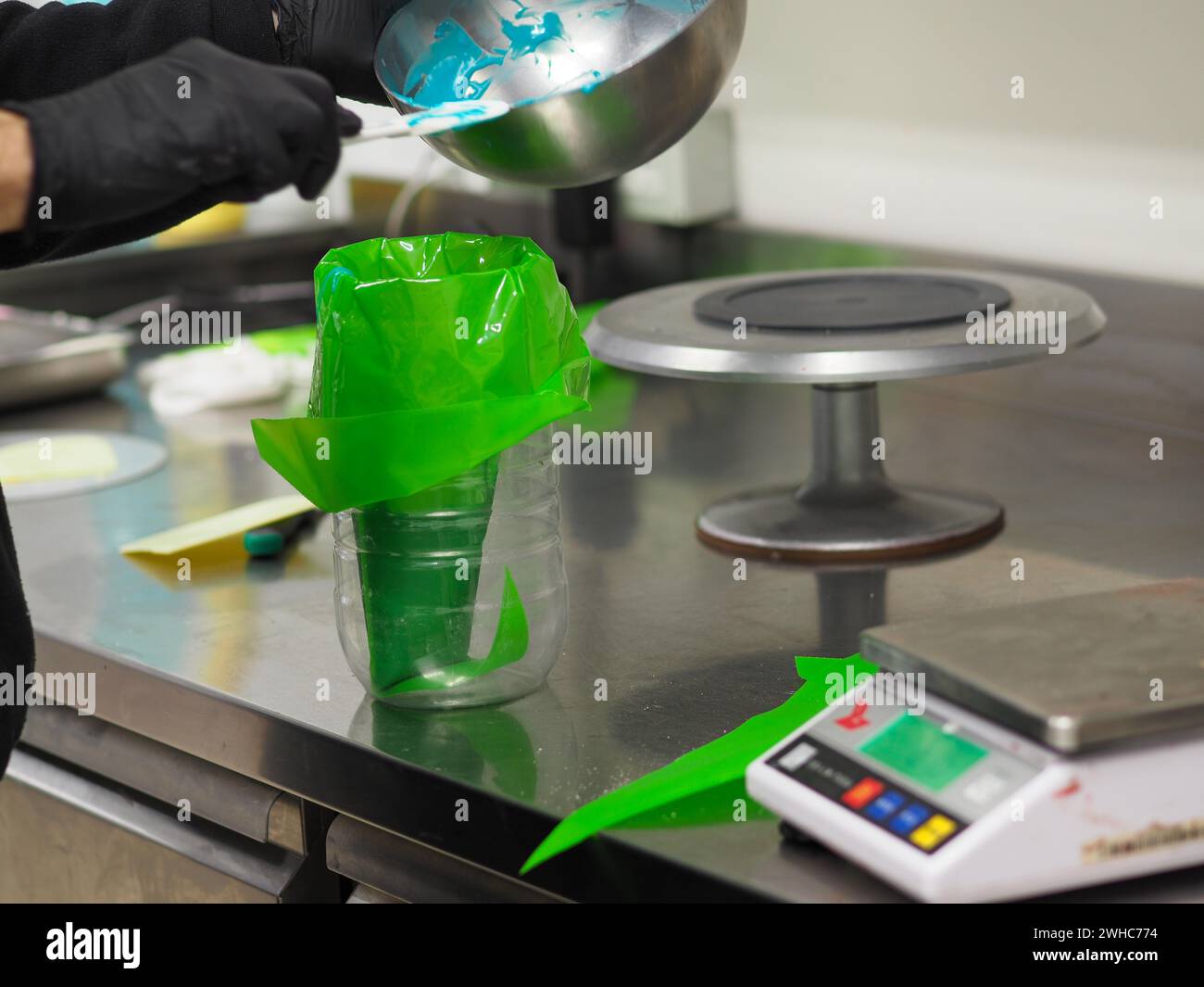 Un fornaio che riempie sapientemente un sacchetto di pasta con glassa verde su una bilancia da cucina Foto Stock