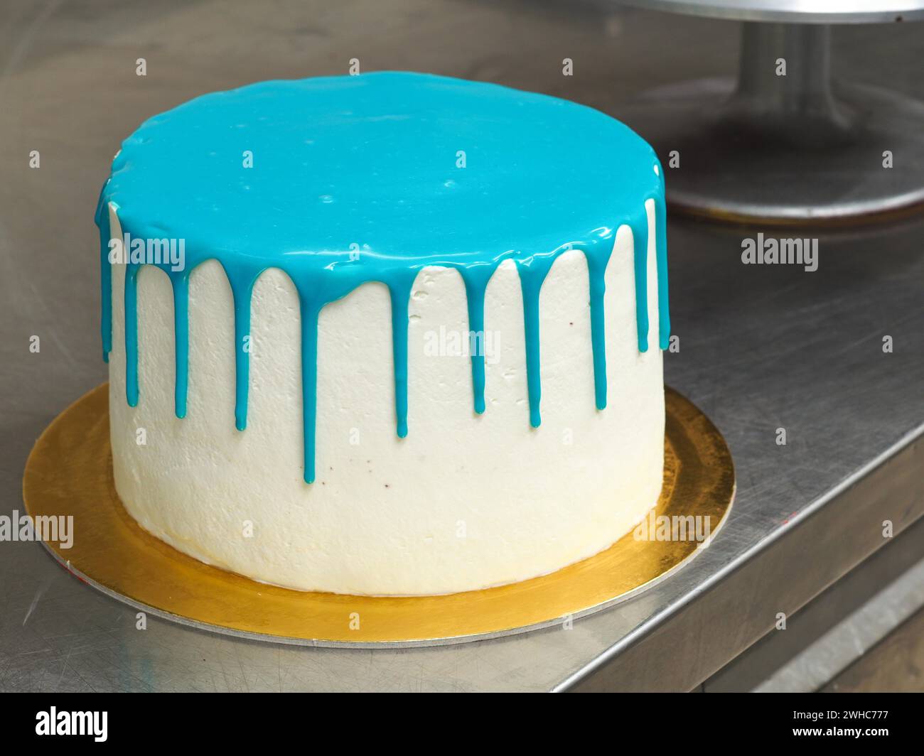 Una torta smerigliata bianca con glassa blu brillante su una superficie in acciaio inossidabile pronta per essere decorata e condita per una festa di compleanno Foto Stock