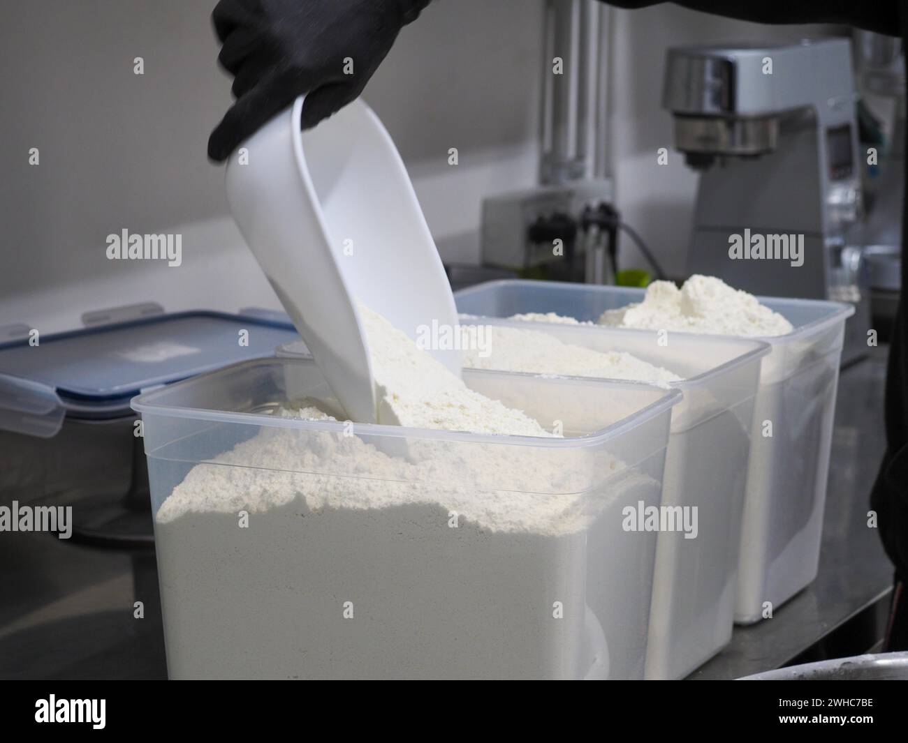 Versare la farina bianca da un grande contenitore con una paletta in una cucina commerciale Foto Stock