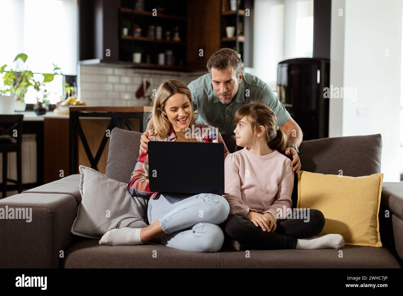 Una famiglia allegra di tre persone trascorre del tempo insieme sul divano del soggiorno, condividendo un momento intorno a un notebook nella loro casa confortevole Foto Stock