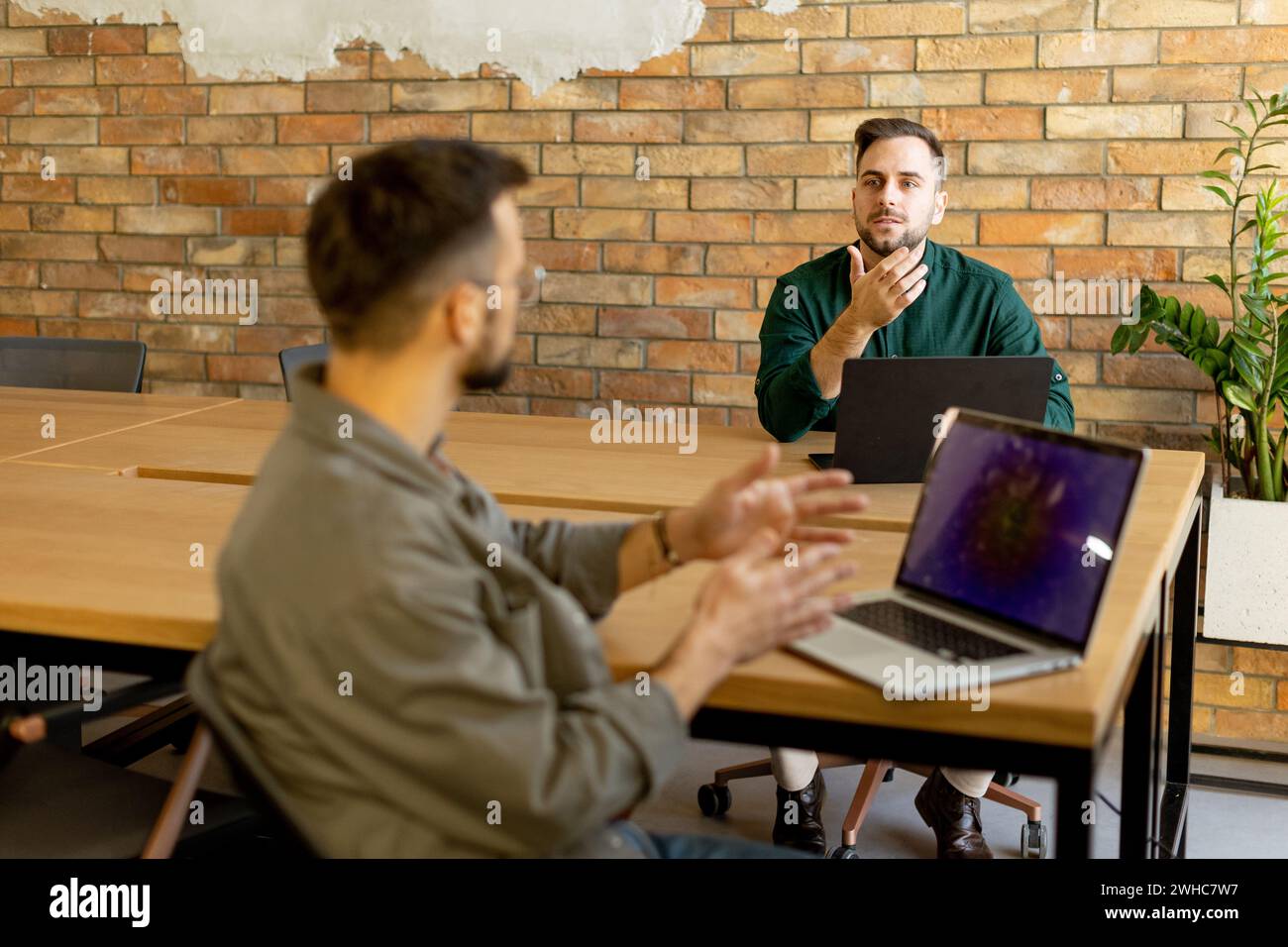 Due professionisti sorridenti si impegnano in una sessione di lavoro collaborativa su un tavolo di legno, il loro cameratismo è evidente in un ambiente da ufficio contemporaneo con un Foto Stock