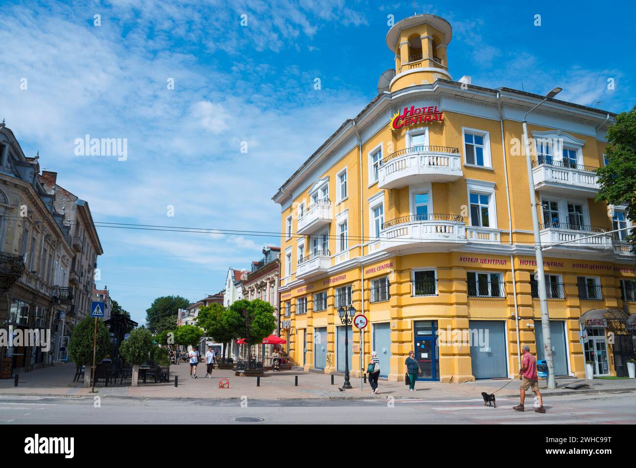 Un edificio alberghiero giallo sotto un cielo azzurro con poche nuvole e passanti sulla strada, hotel nella zona pedonale di Alexandrovska, russe Foto Stock