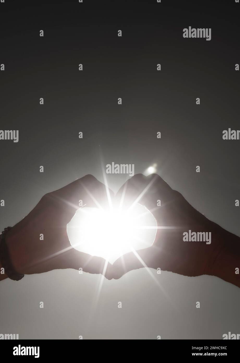 Raggi di luce solare attraverso le mani che formano un cuore Foto Stock