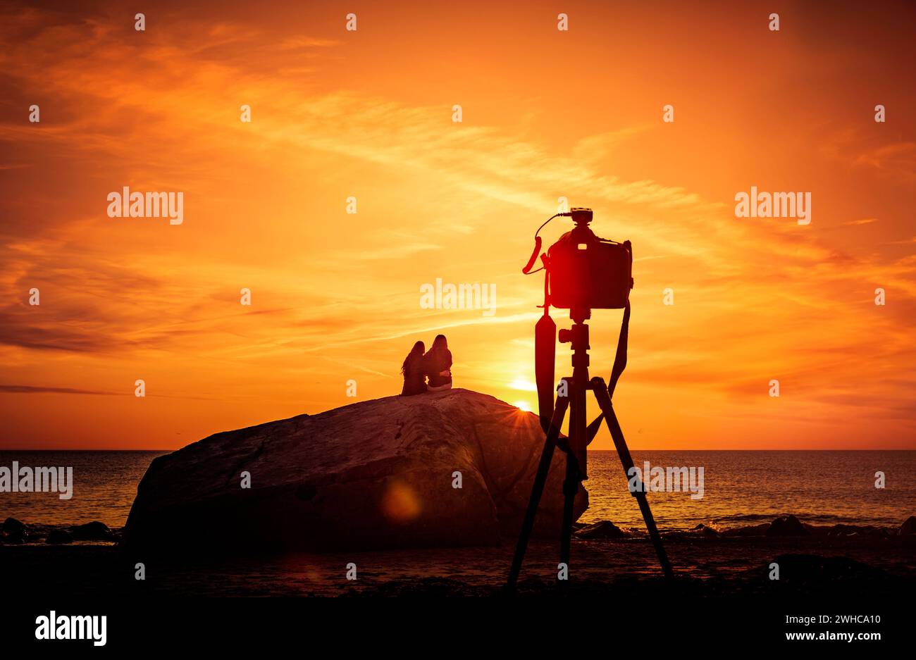 Selfie di una coppia con un treppiede davanti a un tramonto sul mare Foto Stock