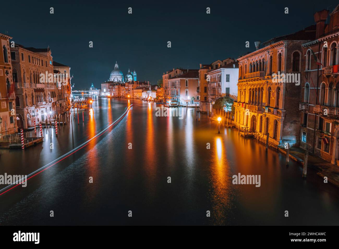 Venezia, scenario notturno d'Italia del Canal Grande di notte. Sentieri luminosi e vivaci di traghetti e barche riflesse sulla superficie dell'acqua. Maestosa Basilica di Santa Maria della Salute sullo sfondo. Foto Stock