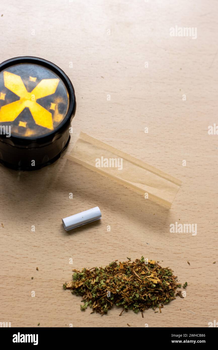 Preparazione di un tema di concetto paraphernalia articolare e droga con trave di erbe utilizzata per macinare i boccioli di cannabis e rotolare le articolazioni di marijuana, accanto alla carta in rotolo Foto Stock