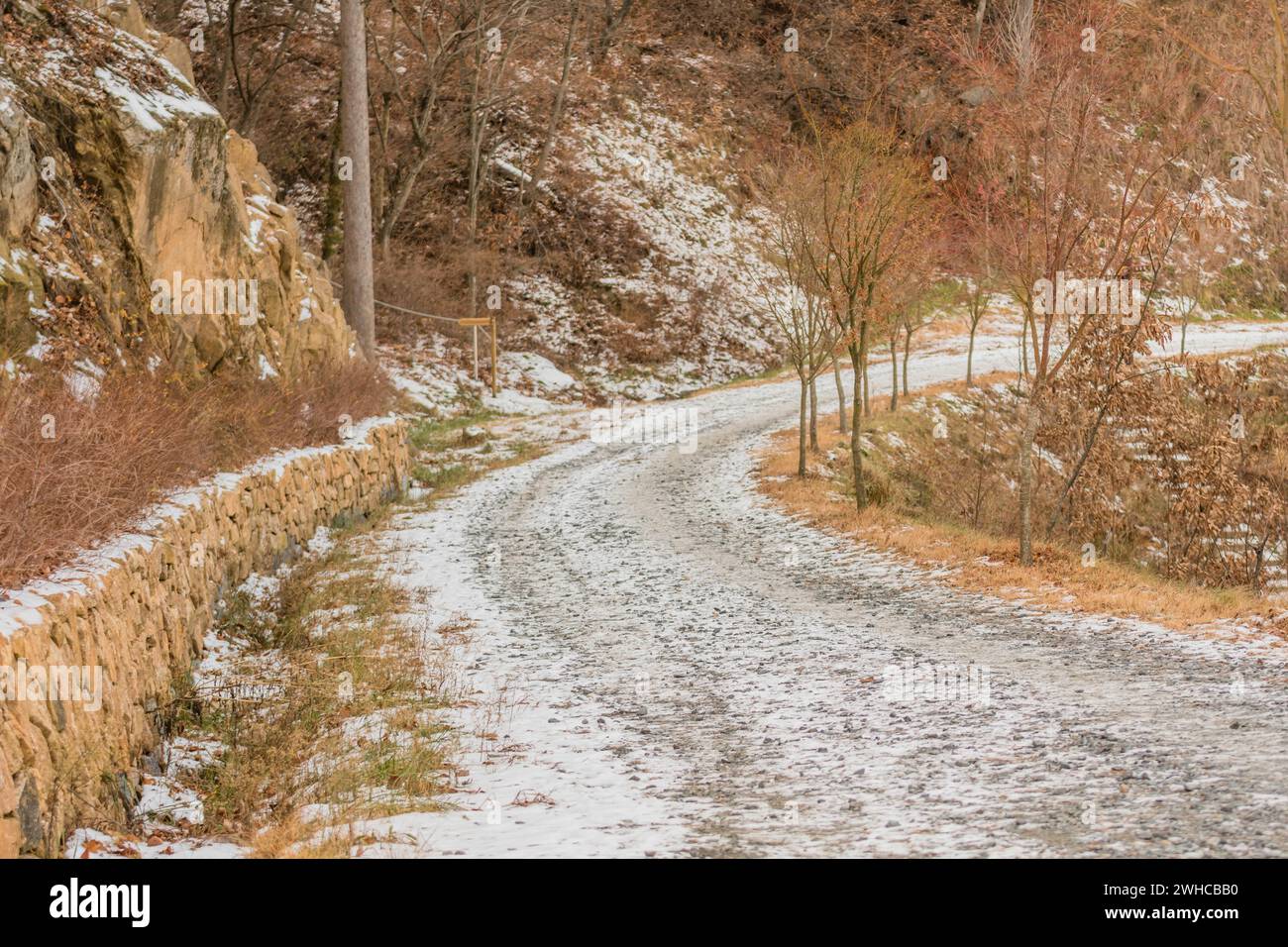 Strada di ghiaia a una corsia laterale sulla montagna con neve a terra nelle soleggiate giornate invernali Foto Stock