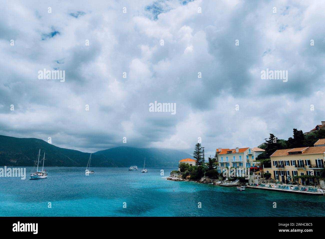 Paesaggio su edifici del villaggio di Fiskardo con tetti in mattoni arancioni. Barche in cerca di riparo nella baia. Isola di Cefalonia Grecia. Foto Stock