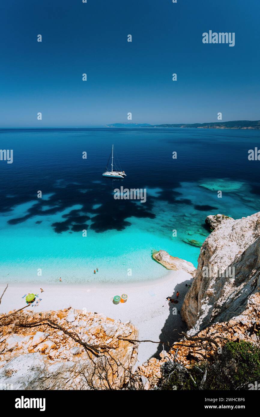 Spiaggia Fteri, isola di Cefalonia Cefalonia, Grecia. Catamarano bianco yacht in un mare azzurro dell'acqua. I turisti sulla spiaggia sabbiosa laguna. Foto Stock