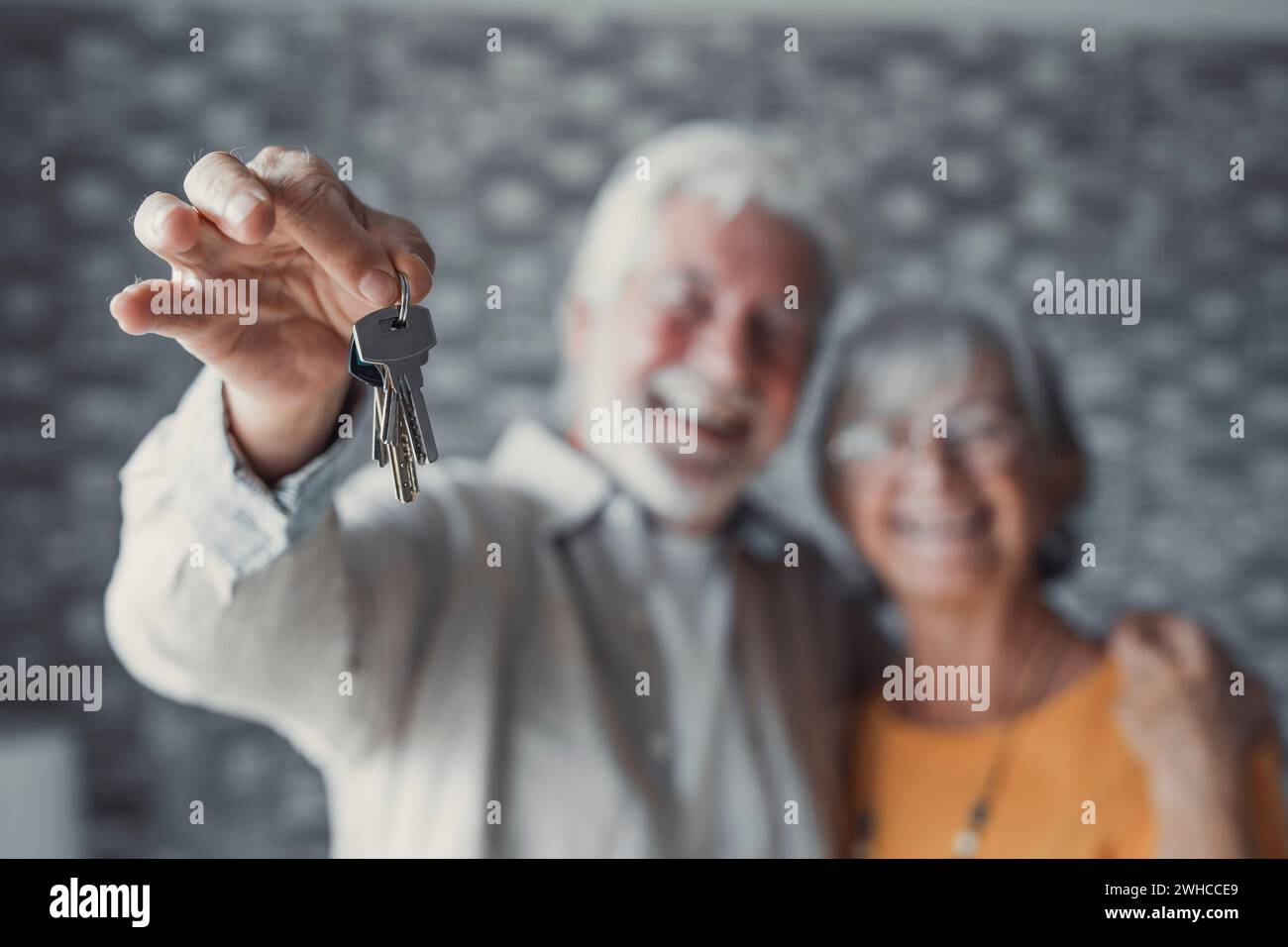Primo piano di una vecchia coppia caucasica felice mostra le chiavi di un appartamento o di una casa. Un uomo e una donna in pensione sorridenti festeggiano il trasferimento in una nuova casa. Trasloco, affitto, concetto immobiliare. Foto Stock