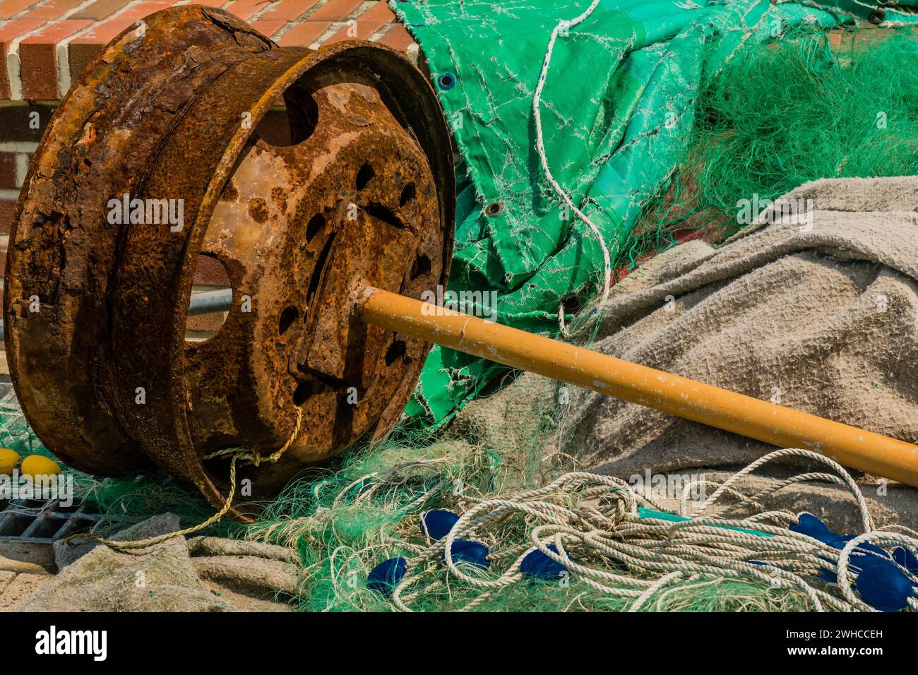 Ruota in metallo arrugginito con canna gialla attaccata tra reti da pesca e detriti in Corea del Sud Foto Stock