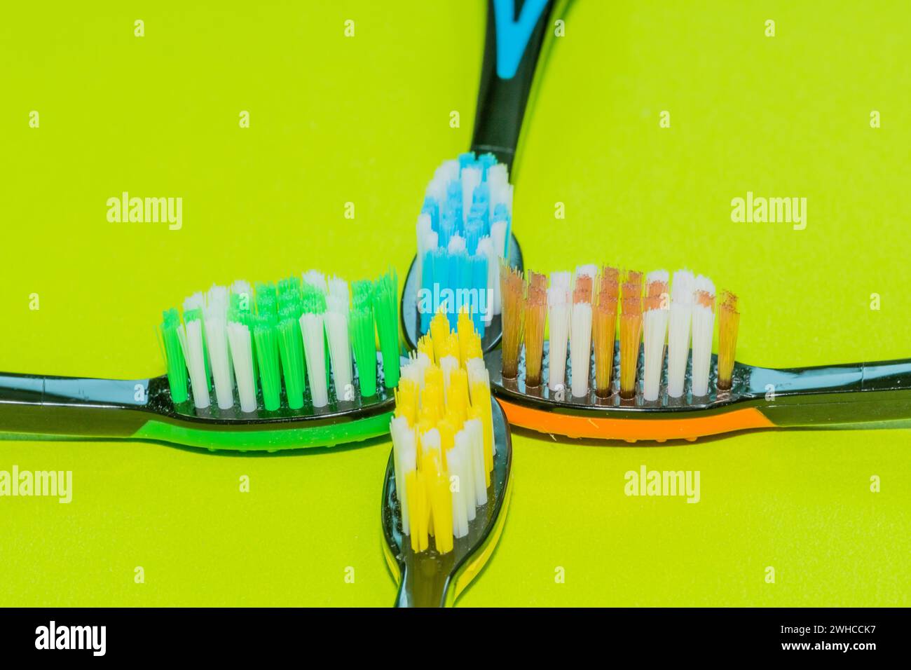 Primo piano di quattro spazzolini da denti in arancione, giallo, verde e blu su sfondo verde Foto Stock