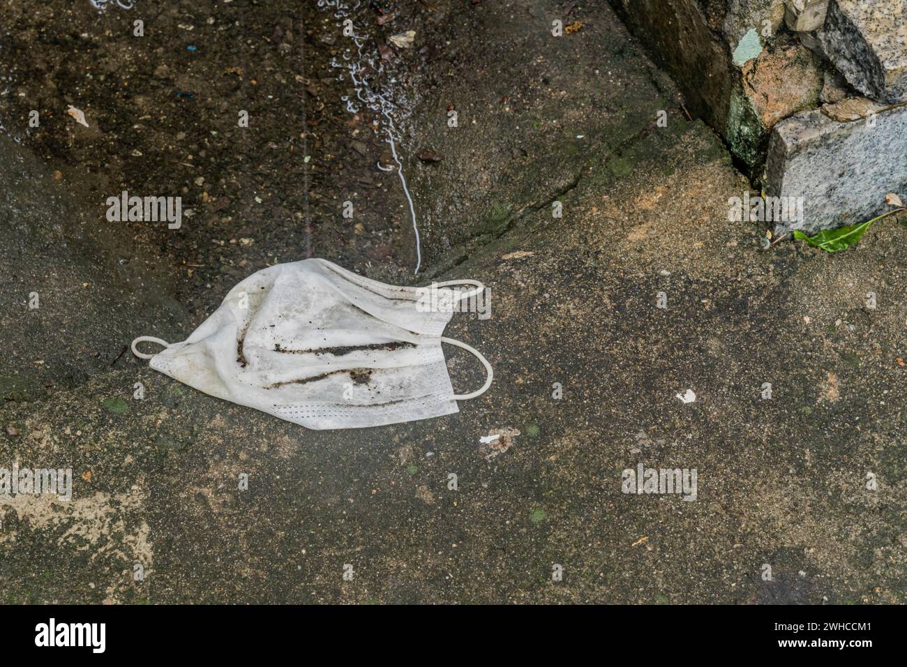 Maschera medica bagnata sporca che posa sul marciapiede accanto alla pozzanghera d'acqua Foto Stock