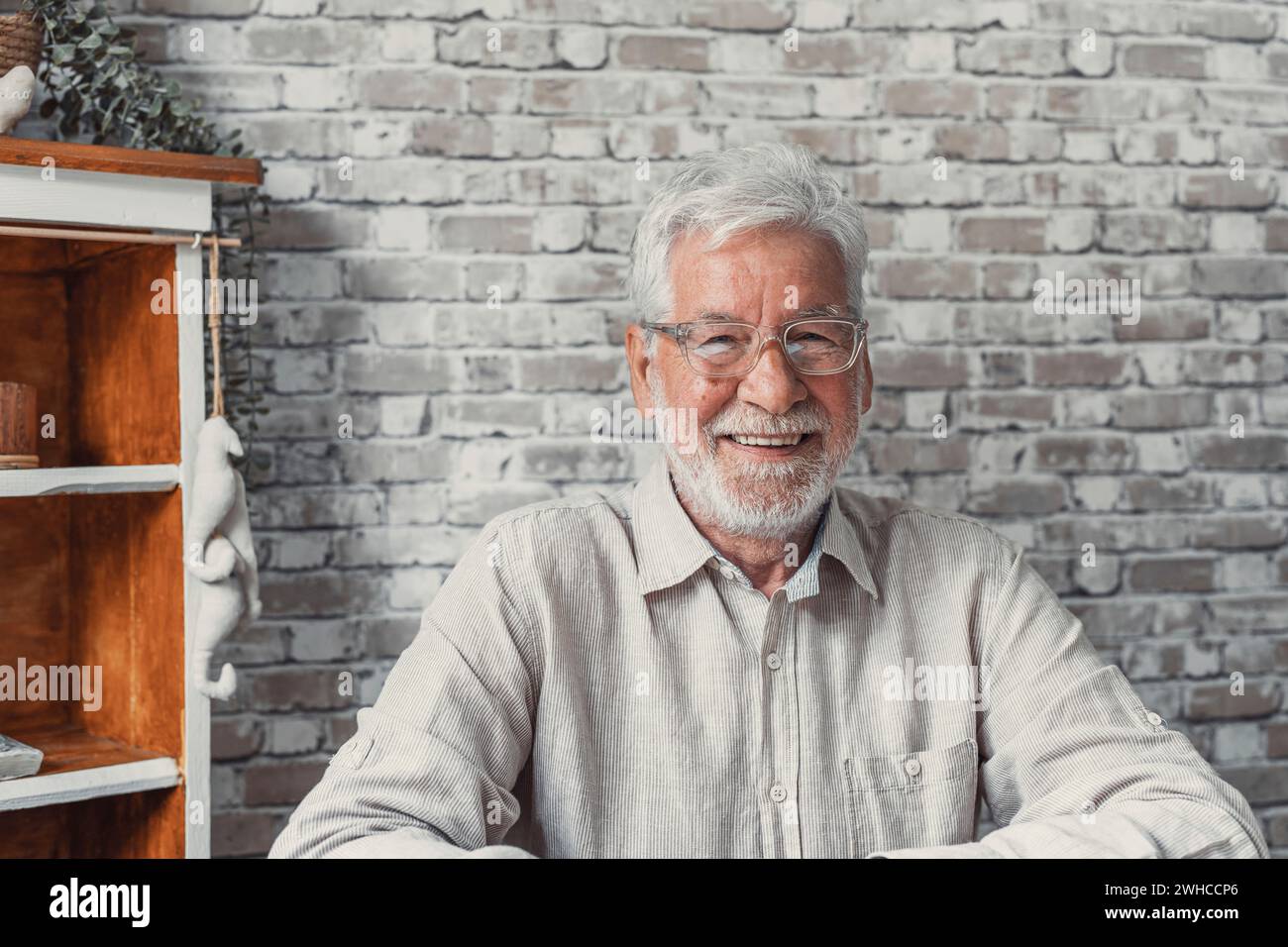 Foto alla testa ritratto bell'uomo anziano ottimista seduto in un ambiente chiuso in posa sulla fotocamera, con un ampio sorriso di spugna pubblicizza i servizi di clinica odontoiatrica professionale per gli anziani. Concetto di pensionamento spensierato Foto Stock