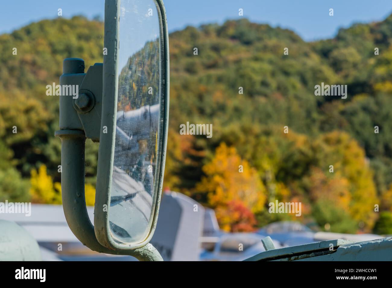 Primo piano dello specchio esterno su un veicolo militare esposto nel parco pubblico con sfondo sfocato Foto Stock