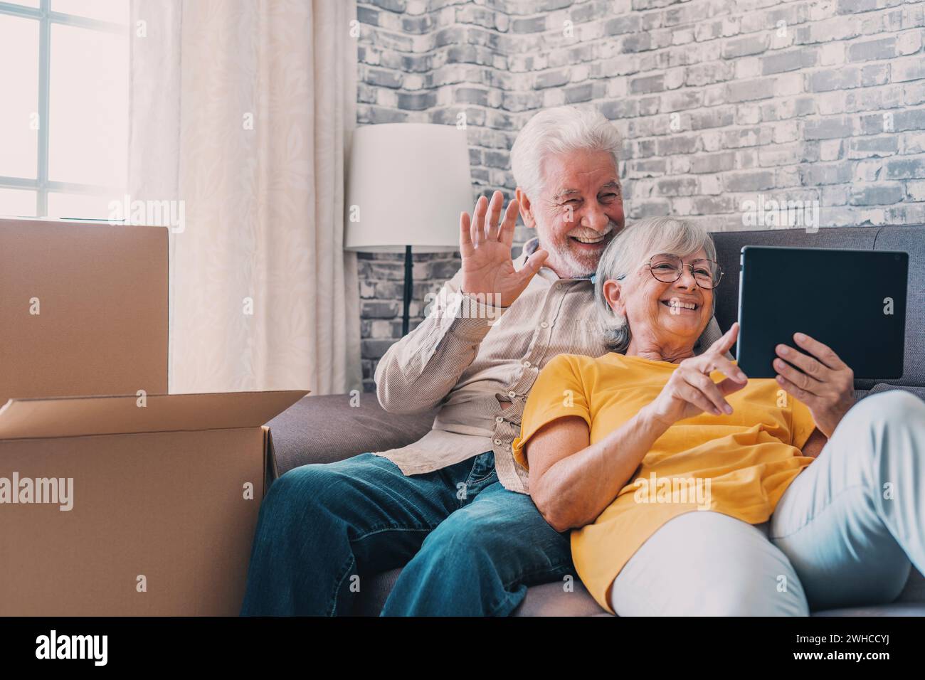 Felice coppia di anziani in pensione che si rilassa sul divano dopo aver traslocato le attività, condiviso il computer tablet, guardando lo schermo, ridendo, videochiamata, utilizzo di app online, servizio Internet Foto Stock