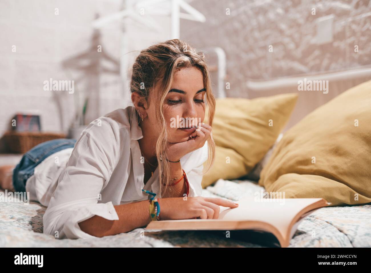 Giovane ragazza caucasica rilassati in una comoda camera da letto leggendo un libro interessante nel fine settimana di casa, riposando donna millenaria sorridente in un letto accogliente goditi il concetto di romanzo, hobby e relax Foto Stock
