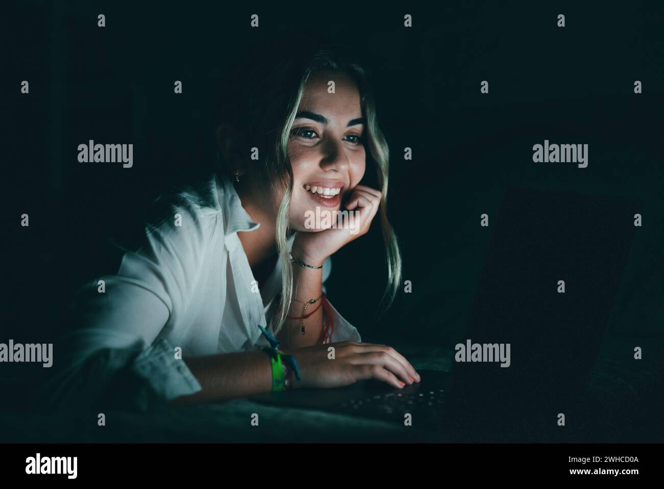 Primo piano, uno studente caucasico sorridente e sicuro di sé che usa il laptop di notte a letto, lavora, termina il progetto a tarda ora, scadenza, guarda lo schermo del computer, siede in camera da letto per i compiti universitari Foto Stock