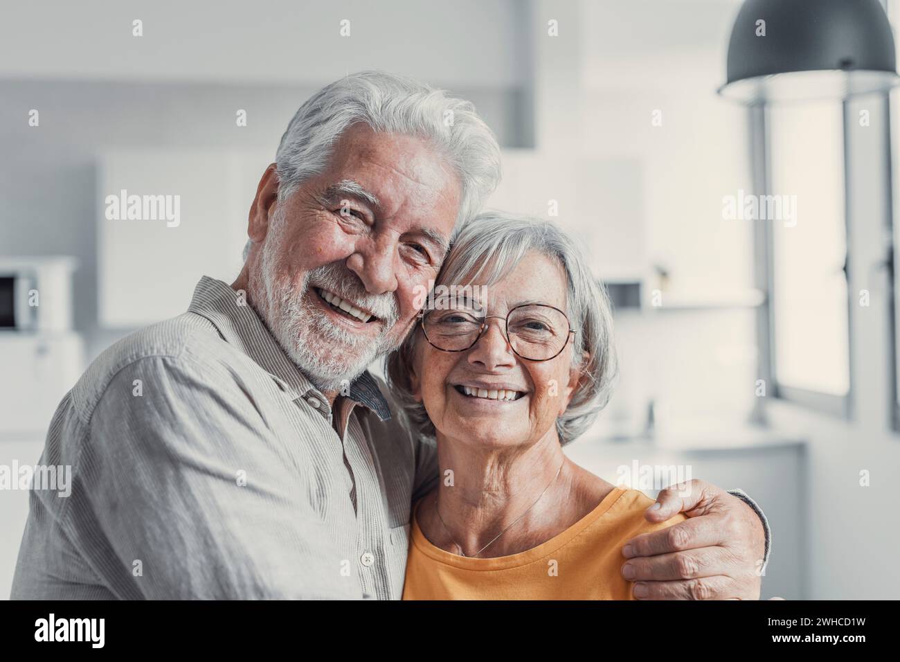 Ritratto alla testa del marito e della moglie degli anni '60 sorridenti in piedi rilassarsi abbracciare coccolare, felice coppia matura riposare in soggiorno abbracciare guardare la fotocamera mostrare amore e cura Foto Stock