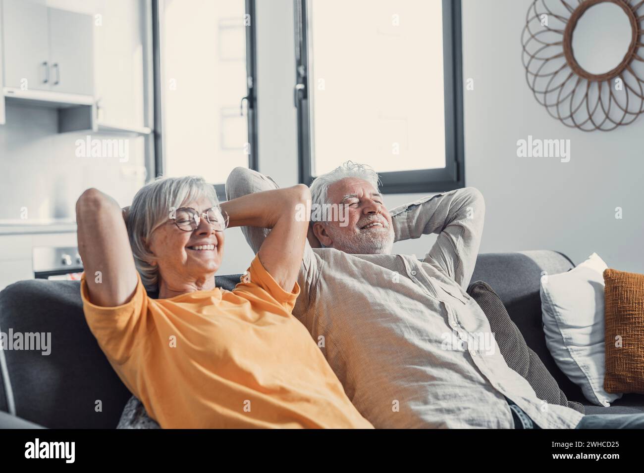 Tranquillo uomo e donna di mezza età con gli occhi chiusi che si rilassano sul comodo divano di casa, famiglia matura che sogna insieme, moglie e marito dai capelli grigi che riposano con le mani dietro la testa, respirando Foto Stock