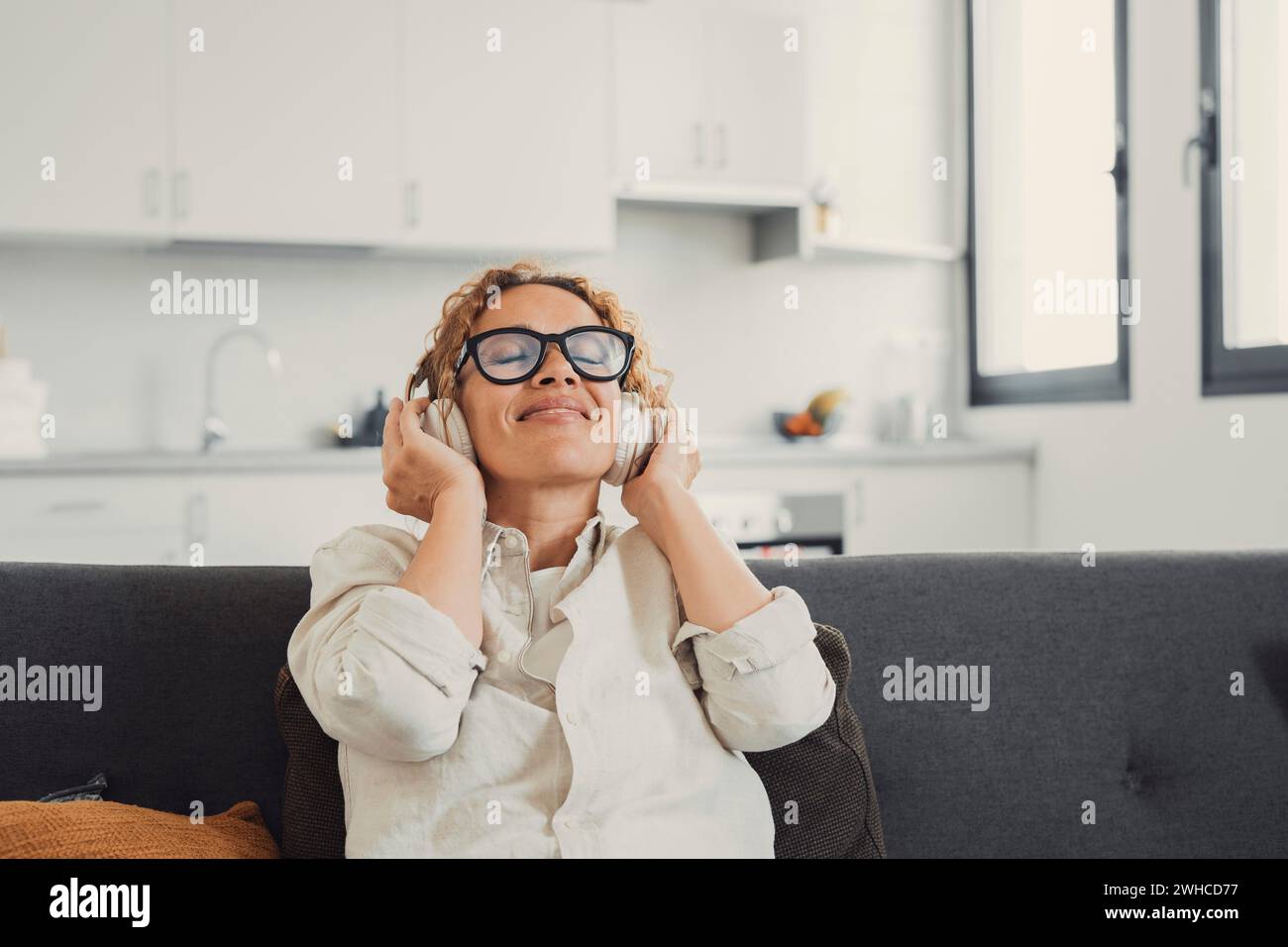 Ragazza tranquilla con le moderne cuffie wireless rilassati sul comodo divano ascoltando la musica, la giovane donna felice e calma con gli auricolari riposa su un comodo divano, goditi un audio di buona qualità e un concetto senza stress Foto Stock