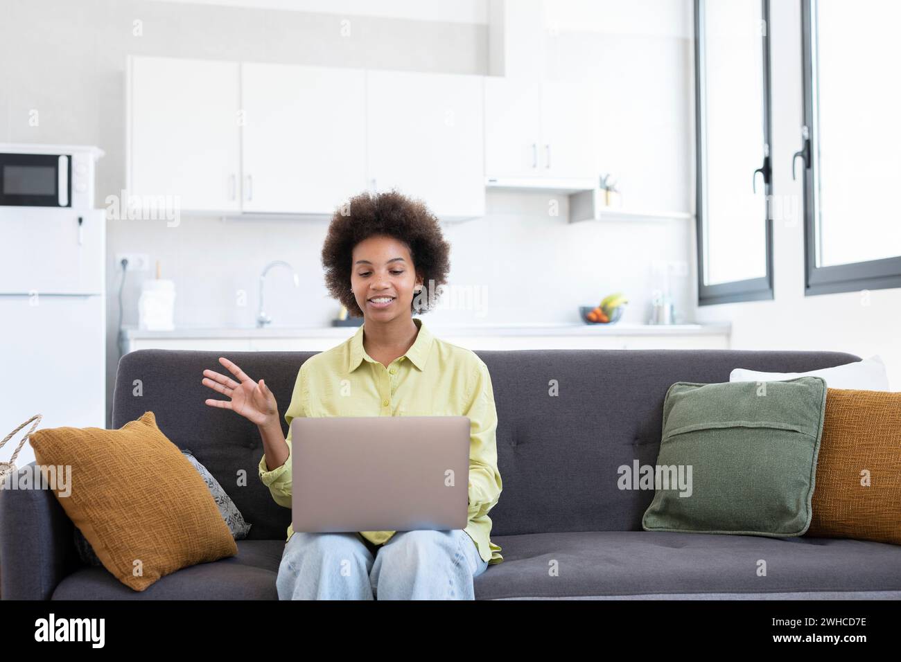 Apprendimento facile. Sorridente giovane donna di corsa mista sedersi sul divano cercare informazioni utilizzando il laptop guardare la lezione video del webinar. Una donna nera positiva utilizza il servizio di istruzione online per migliorare le abilità Foto Stock