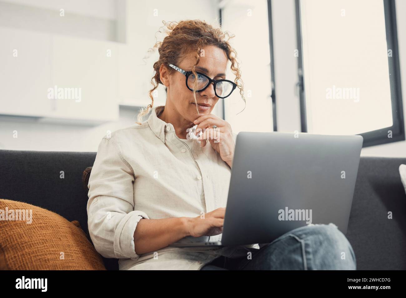 Giovane donna sorridente che usa il computer portatile, seduta sul divano a casa, bella ragazza che fa shopping o chatta online sui social network, divertendosi, guardando film, freelance che lavora su progetti informatici Foto Stock