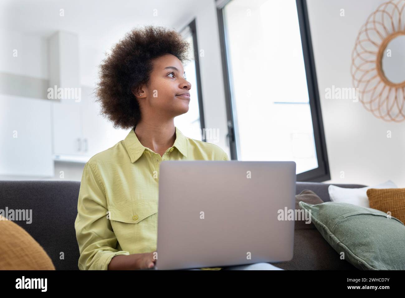 Giovane donna nera sorridente che usa il computer portatile, riposa sul comodo divano, parla in videochiamata, chatta online, naviga su Internet, guarda film, fai shopping su Internet. Utente di gadget digitali pigri Foto Stock