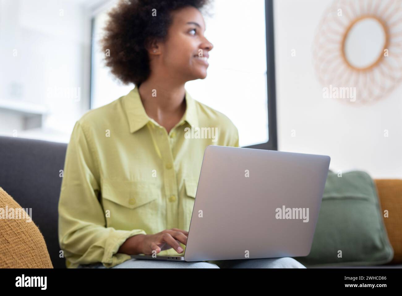 Giovane donna nera sorridente che usa il computer portatile, riposa sul comodo divano, parla in videochiamata, chatta online, naviga su Internet, guarda film, fai shopping su Internet. Utente di gadget digitali pigri Foto Stock