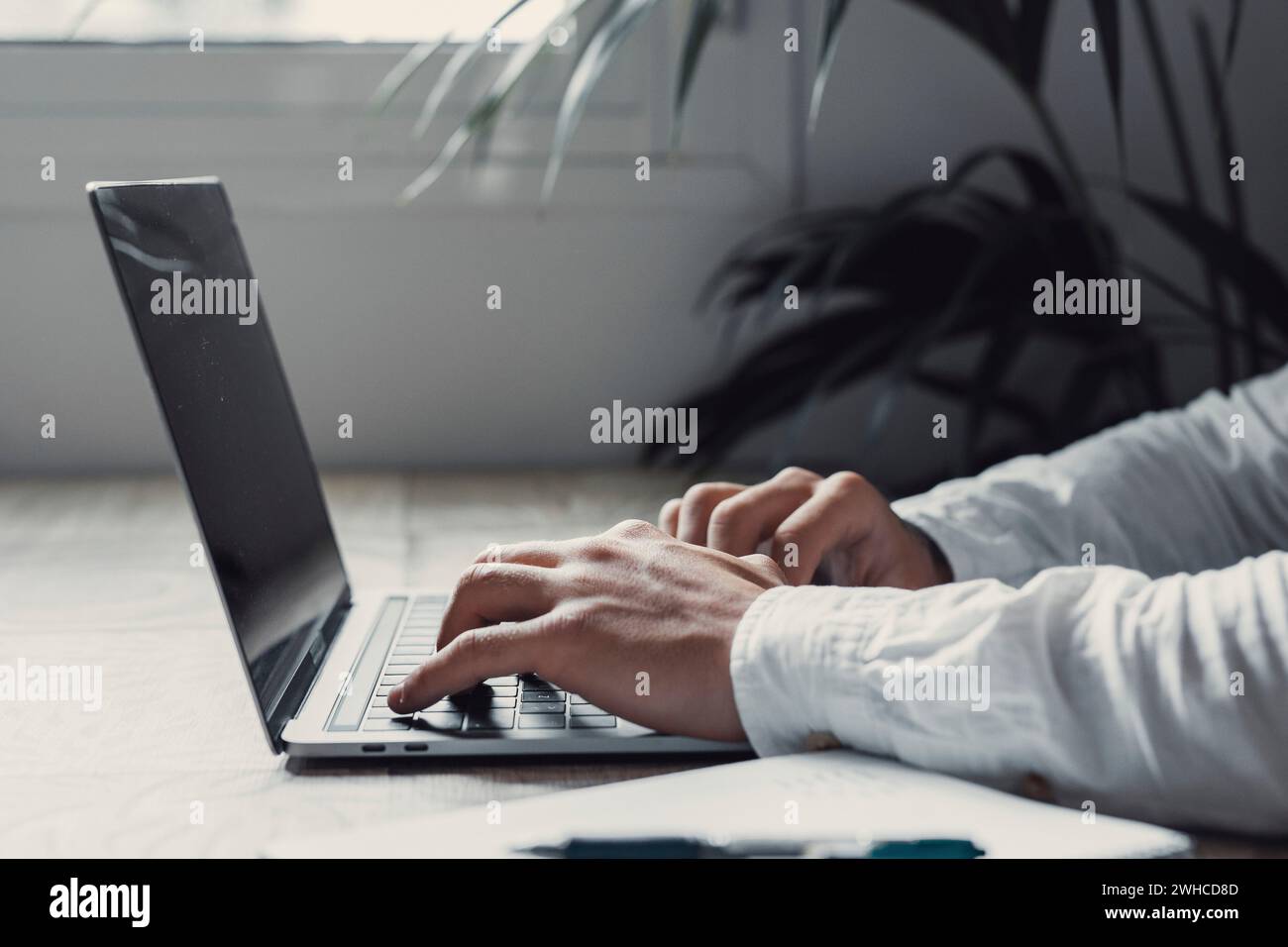 Vista laterale e ravvicinata, bellissimo giovane uomo d'affari che lavora con il computer in remoto, seduto al tavolo di legno in ufficio. Ritrarre e chiudere le mani scrivendo e scrivendo sul laptop che lavora. Foto Stock