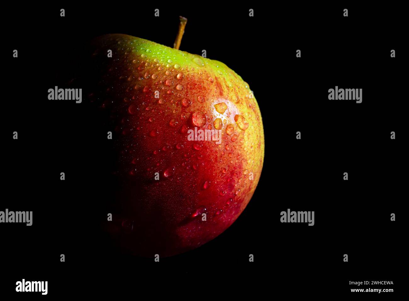 Mela rossa con macchie verdi e goccioline d'acqua, sfondo scuro Foto Stock