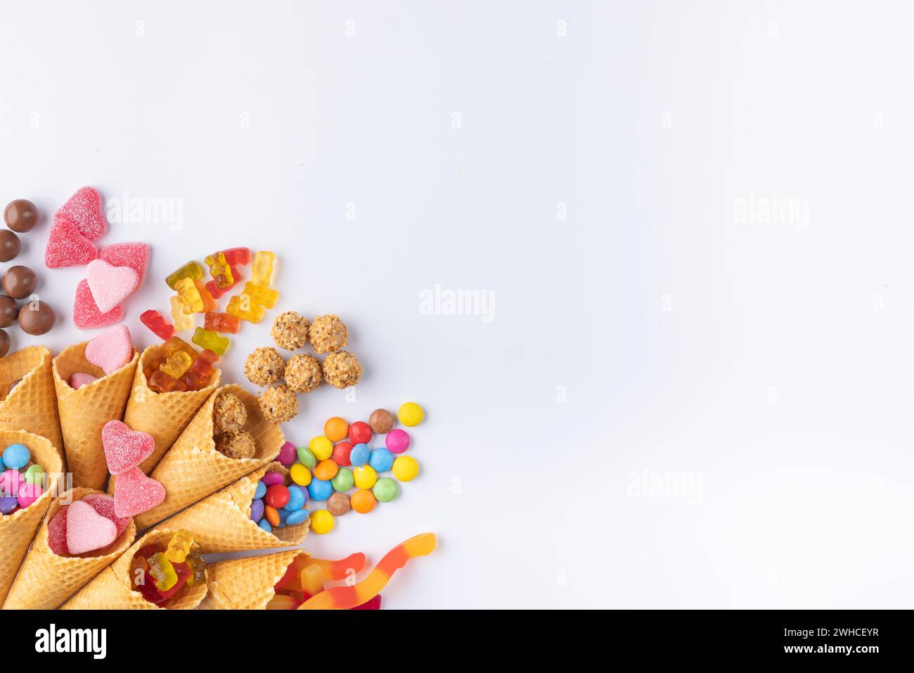 Dolci colorati, orsetti gommosi, lenticchie di cioccolato che cadono dai coni del gelato, stanza delle copie, sfondo bianco Foto Stock